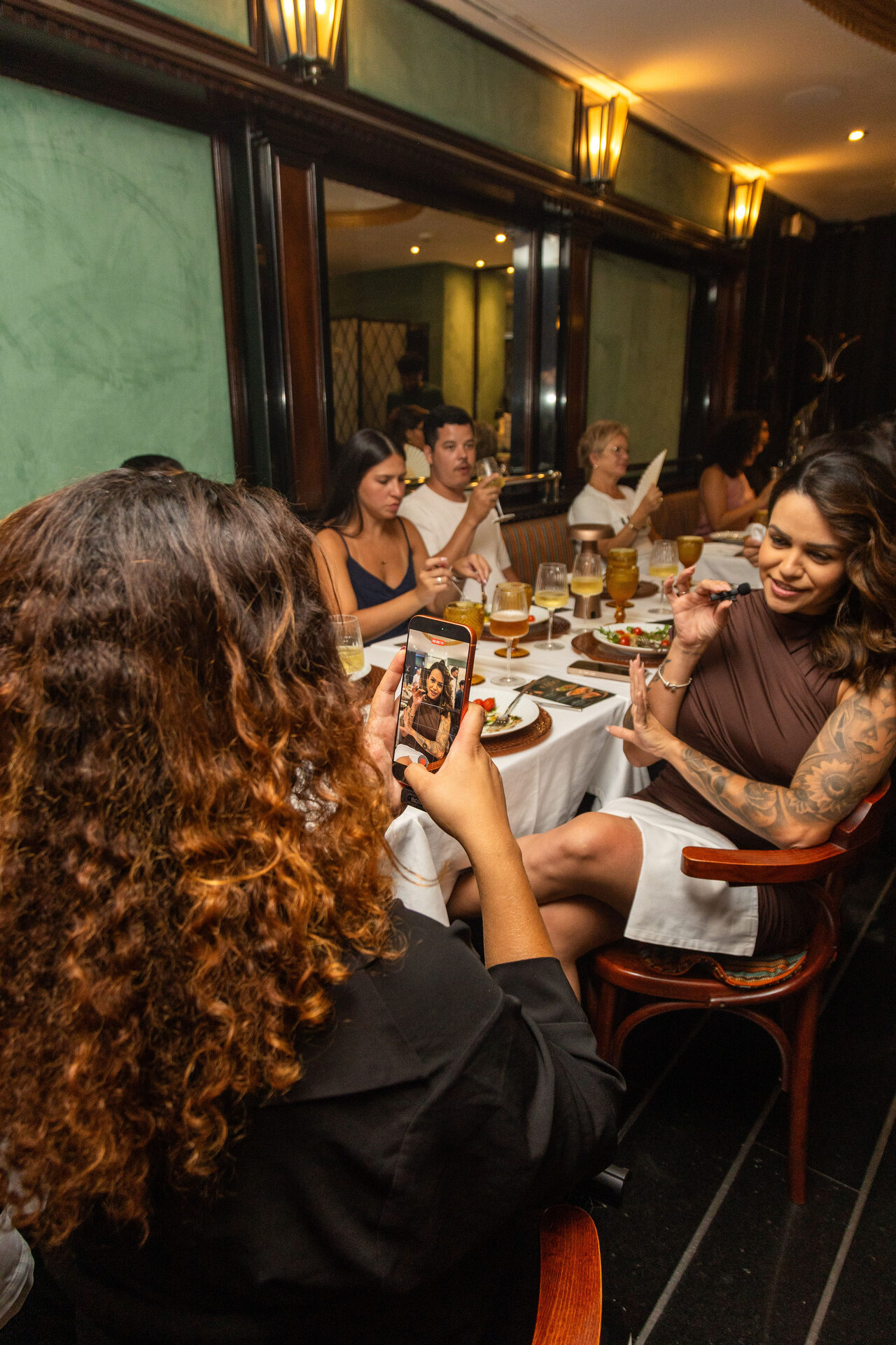 Priscila a fotografar uma convidada com o telemóvel, durante um jantar de evento